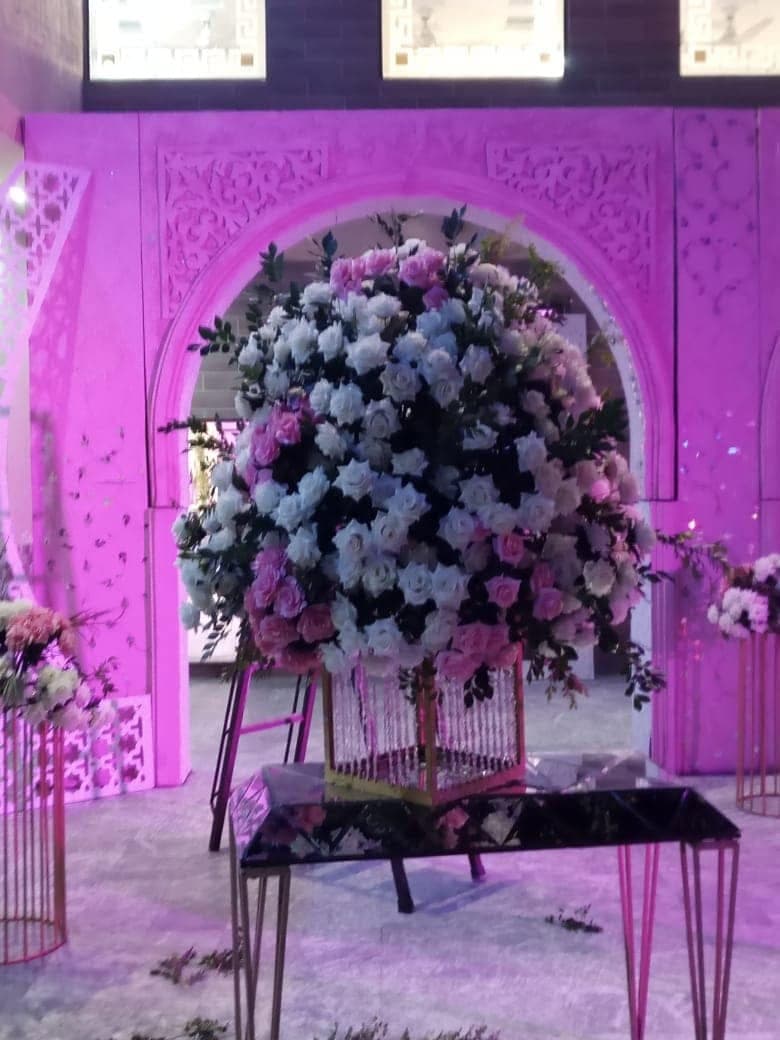 Tall floral urn arrangement lit in violet beneath an ornamental arch