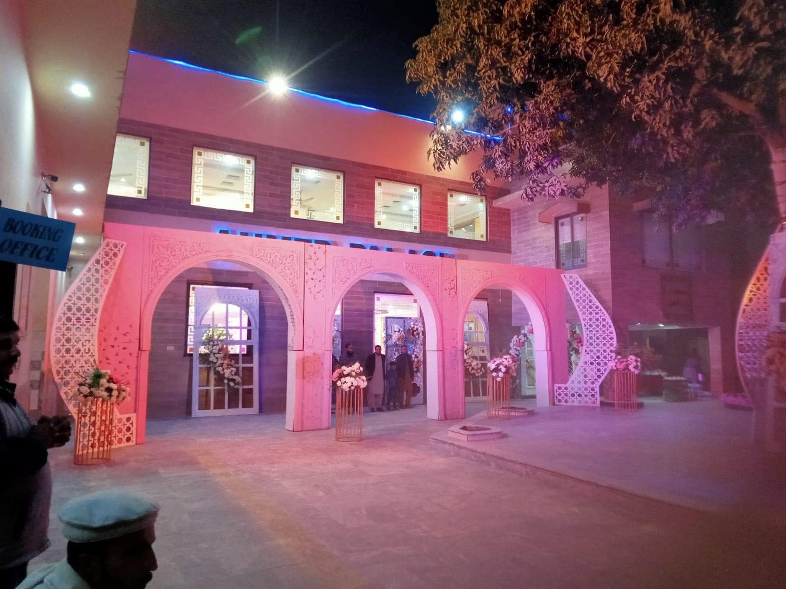 The arched façade of Ahmed Palace lit in warm pink light after dark, Mughalpura, Lahore