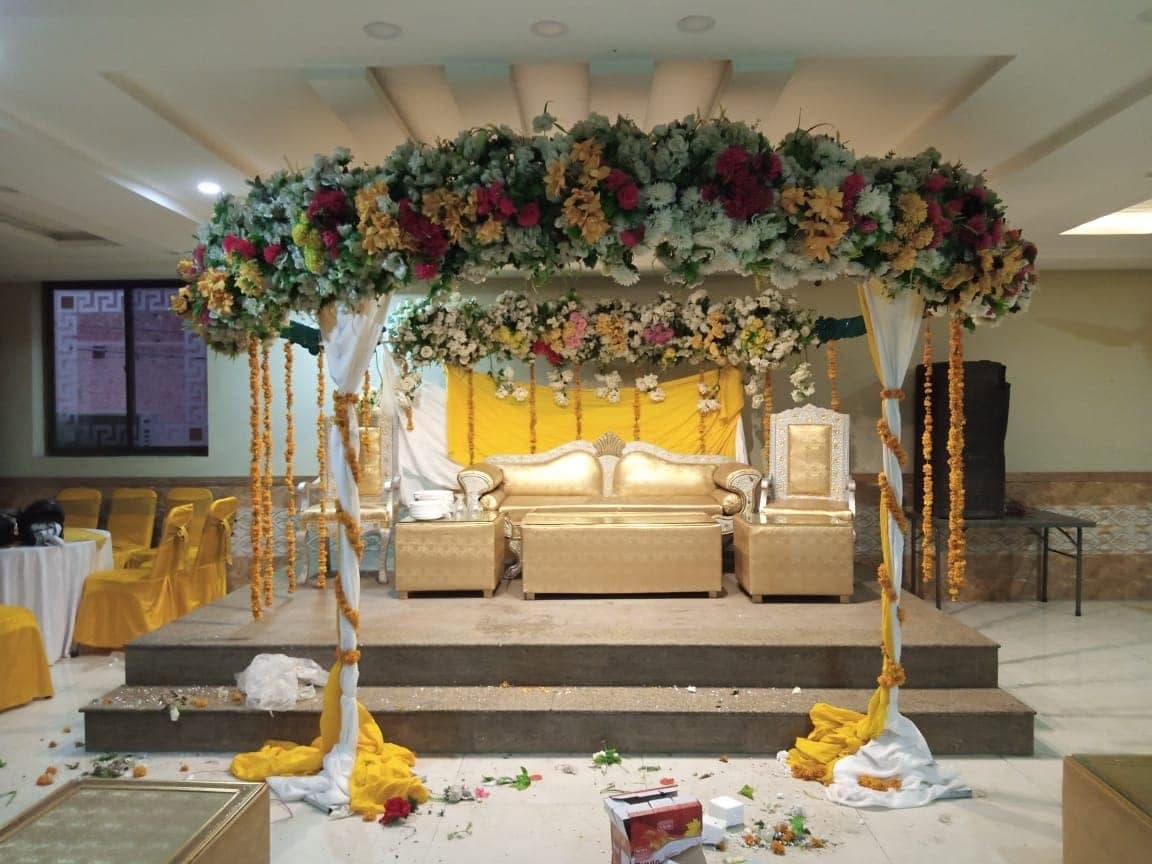 Mehndi stage decorated with marigold strings and a floral canopy over low gold seating